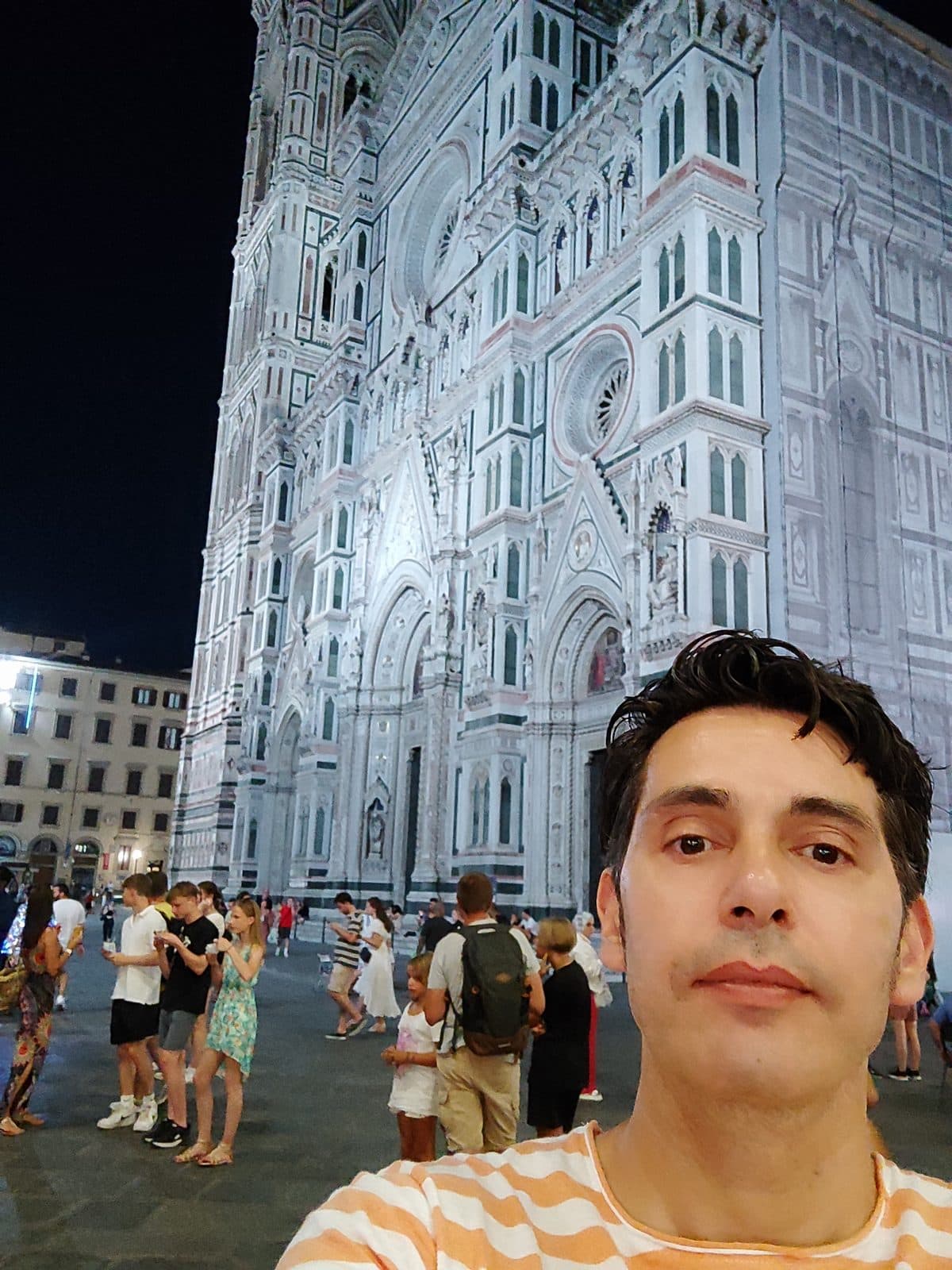 The marble facade of Florence Cathedral lit at night with visitors in the square