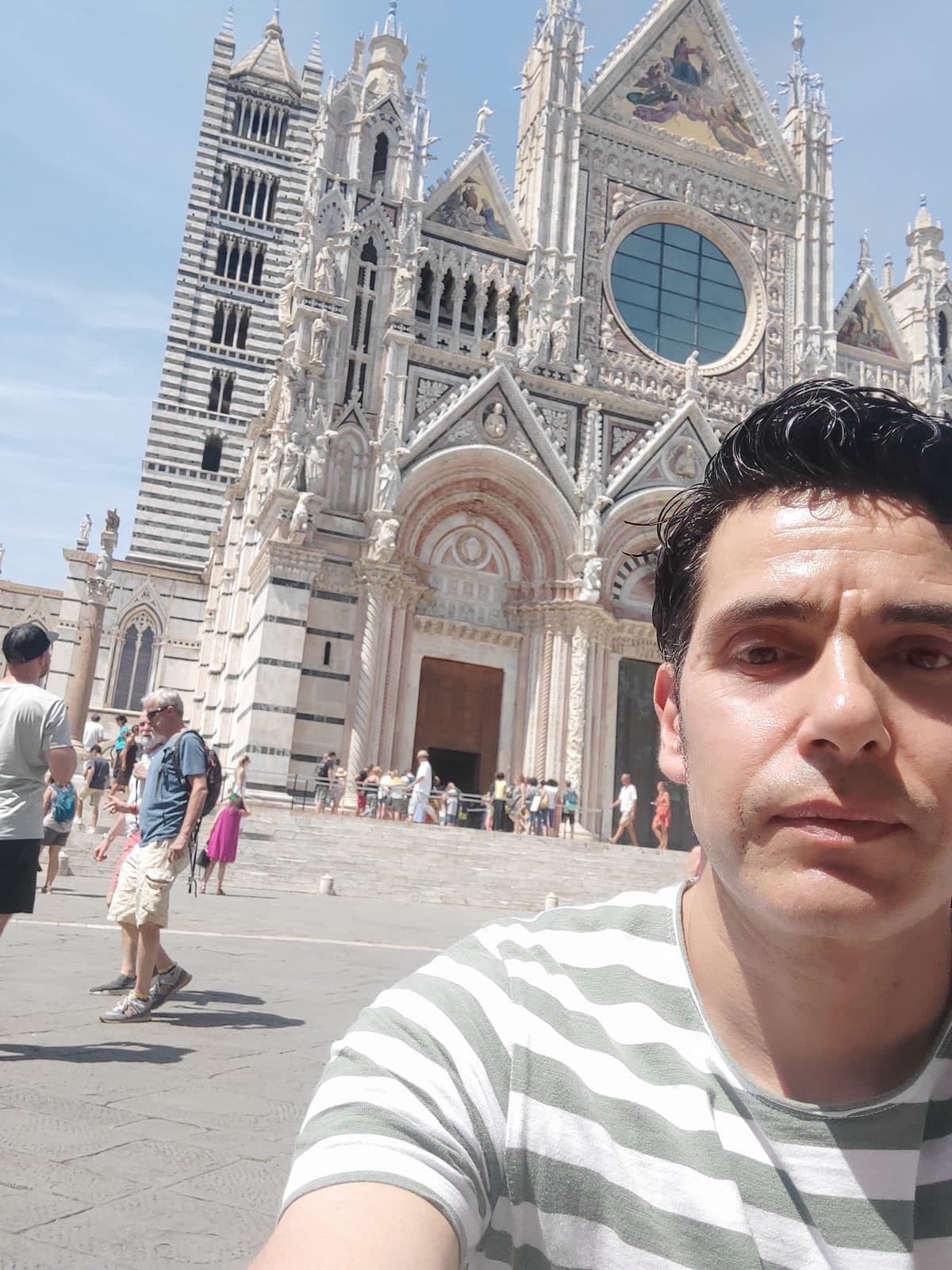 The west facade of Siena Cathedral in striped marble with visitors on the piazza