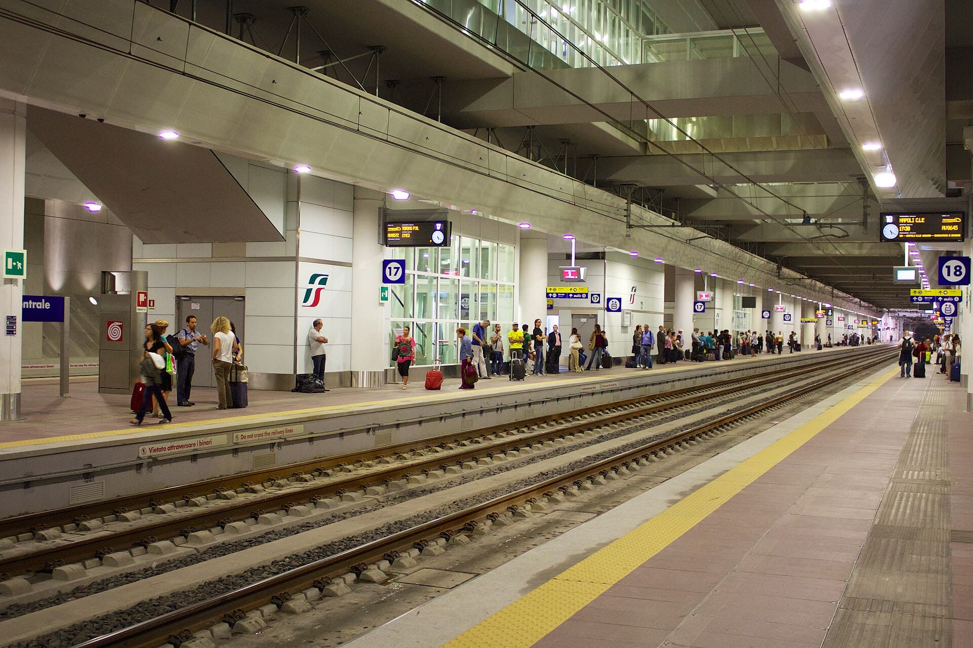 The underground high-speed platforms 17 and 18 at Bologna Centrale, with passengers and suitcases waiting along a long lit platform and departure boards overhead