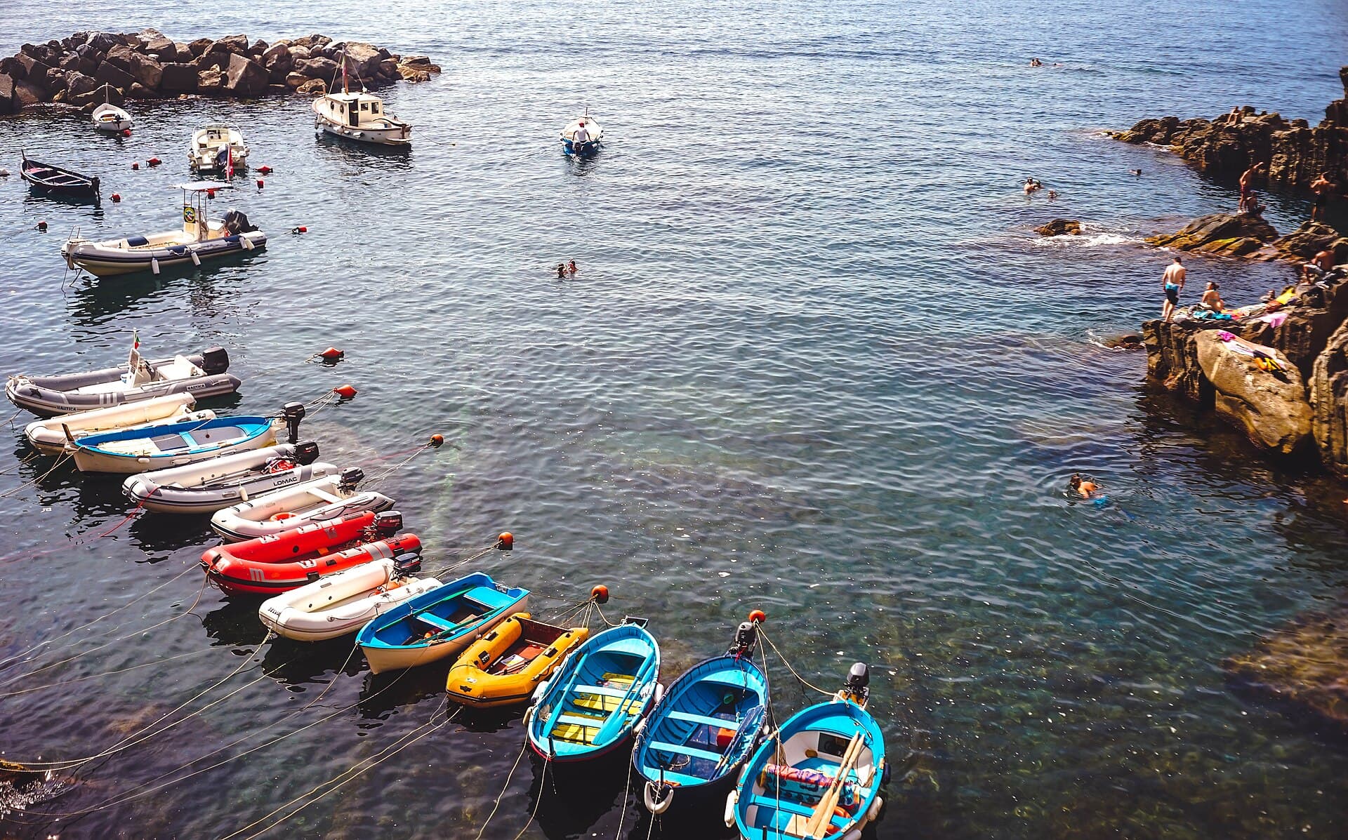 The small harbour at Riomaggiore, with dinghies moored in a rocky inlet and swimmers on the rocks