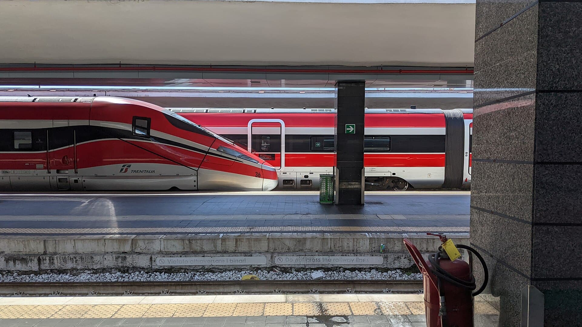 Two red and white Frecciarossa 1000 high speed trains standing at adjacent platforms under the roof of Napoli Centrale station