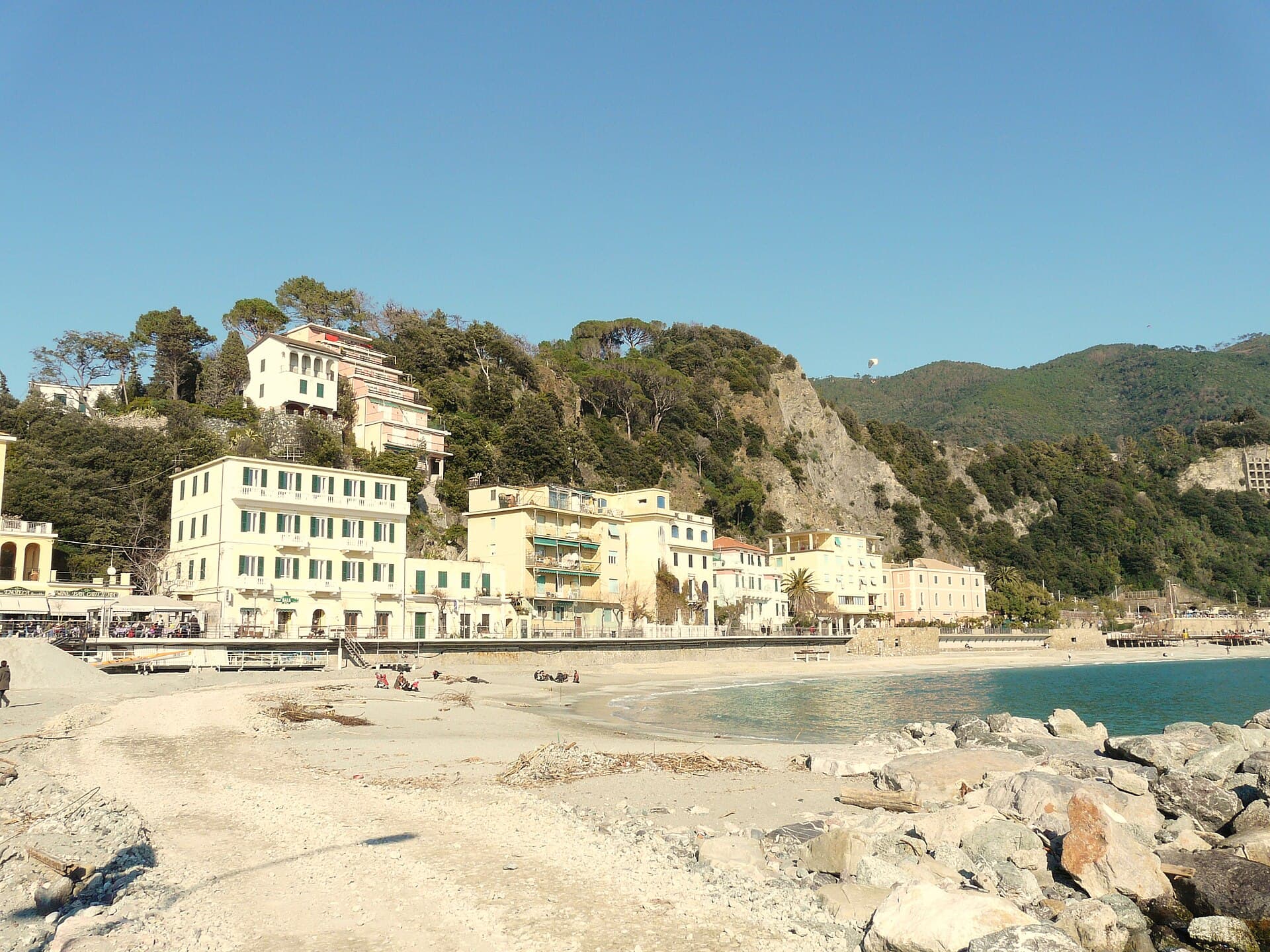 The Fegina beach at Monterosso out of season, wide pale sand with winter debris, pastel buildings along the seafront and a pine covered headland behind